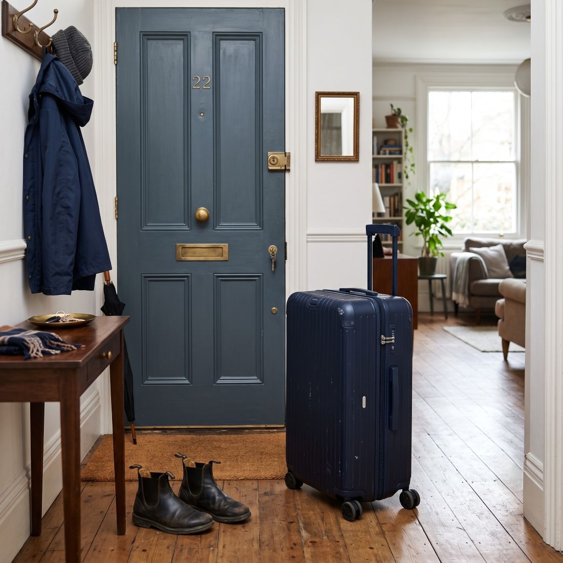 A large, modern hard-shell wheeled suitcase stands upright beside the inside of the front door